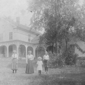Historic, black and white photo of two women and two children standing in front of a white farmhouse in Chatham, New York.